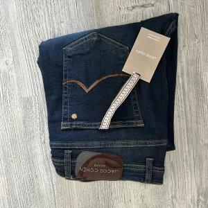 Mörkblå jeans från Jacob Cohen - Snygga mörkblå jeans från Jacob Cohen med klassisk femficksdesign, kontrastsömmar och läderpatch bak. Jeansen har en smal passform och är tillverkade i mjukt denimtyg med stretch för extra komfort. Perfekta för dig som gillar stilrena och exklusiva jeans. Storlek 40, priset går att diskutera 