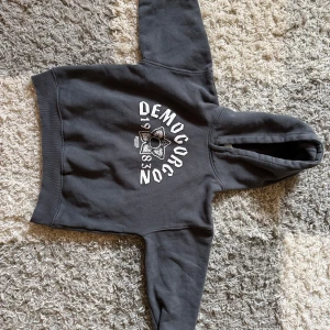 Stranger Things hoodie från Zara - Mörkgrå hoodie från Zara x Stranger Things med tryck av Demogorgon och text framtill. Baksidan har en stor röd patch med coolt mönster och Demogorgon-motiv. Mjuk insida, huva och långa ärmar. Perfekt för dig som älskar serien och vill sticka ut.