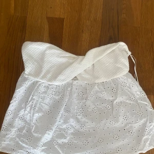 Vit axelbandslös broderad tubtopp - Supersöt vit tubtopp från Gina Tricot med twistad överdel och broderade blommor i tyget. Toppen är axelbandslös. 