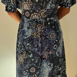 Blommig långklänning Odd Molly - Supersnygg långklänning från Odd Molly med blått och beige blommönster. Klänningen har omlottliv, bred midja och korta ärmar. Lätt och flowy känsla, perfekt för vår och sommar. Snygga detaljer med knytband och pärlor. Använd 2ggr! Nyskick !