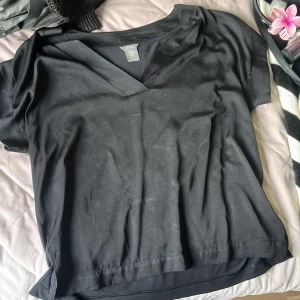 Svart v-ringad topp från Lindex - En svart, enkel och stilren topp från Lindex i storlek M. Toppen har v-ringning och korta ärmar, perfekt för en clean och avslappnad look. Tillverkad i mjuk bomull som känns skön mot huden. Passar dig som gillar basic men ändå vill ha något snyggt.