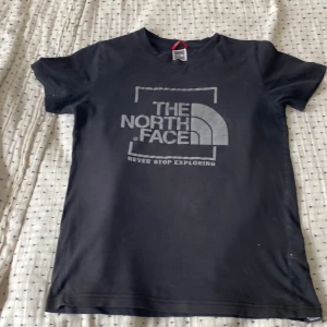 Svart t-shirt från The North Face - Svart t-shirt från The North Face med stor logga och texten 'Never Stop Exploring' på bröstet. Klassisk passform med rund hals och korta ärmar. Tillverkad i mjuk bomull, perfekt för en chill och sportig stil.