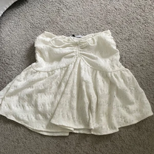 Vit kortkjol med snörning - Superfin vit kortkjol med broderade detaljer och snörning i midjan. Kjolen har en lätt volang och är gjord i ett luftigt material som passar perfekt till varma dagar. Söt och trendig modell som ger en fräsch look. Shorts under kjolen!