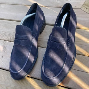 Mörkblå mocka loafers från Boggi Milano - Snygga mörkblå loafers i mocka från Boggi Milano. Klassisk design med rund tå och platt sula, perfekt för en stilren look. Tillverkade i Italien med fina detaljer och bekväm passform. Storlek 43 1/2