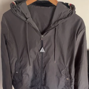 Grå vindjacka från Moncler - Säljer en Moncler Windbreaker till riktigt bra pris! Har ingen användning för den längre, så den får gärna komma till någon som uppskattar den. Passformen är perfekt och den sitter riktigt snyggt på! Storlek M, men passar även som S beroende på hur man vill att den ska sitta.  Jackan har självklart QR-kod som går att skanna, dessutom på Moncler-loggan.  Pris: 2200 kr – men kan diskuteras vid snabb och smidig affär. Hör av dig vid intresse!
