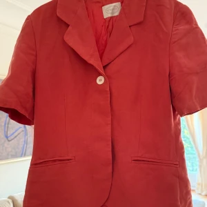 Kavaj med korta ärmar från New House  - Fin kavalj i tegelröd färg. Gömda knappar. Igensydda fickor