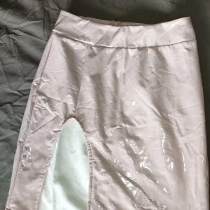 Glansig ljusrosa kjol med slits party rave - Säljer en glansig ljusrosa kortkjol med hög midja och en cool slitsl. Kjolen har en figurnära passform och dragkedja bak. Perfekt för dig som vill sticka ut med en unik look. Tror den är från Pretty little things men den saknar lapp.