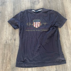 Mörkblå GANT t-shirt med tryck - Snygg mörkblå t-shirt från GANT med stort tryck framtill och klassisk rund hals. T-shirten har korta ärmar och är gjord i mjuk bomull. Perfekt för dig som gillar sportig och stilren look med amerikansk vibe.
