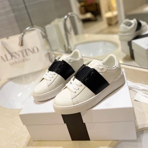 Valentino Garavani Open sneakers med svart band - Snygga vita sneakers från Valentino Garavani med ett brett svart band över vristen och nitar på hälen. Skorna har rund tå, platt sula och är tillverkade i skinn. Perfekta för dig som gillar stilrena och exklusiva sneakers. De flesta storlekar finns tillgängliga. Leverans sker inom 12–15 dagar.