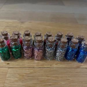 Glitter i små glasflaskor - Glitter i små flaskor! 16 stycken i färgerna: grön, rosa, silver, ljusblå, mörkblå, röd, guld och mörkare rosa. Oanvända!