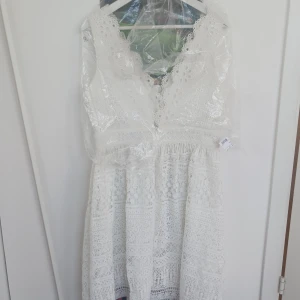 Vit spetsklänning med v-ringning - Superfin vit klänning med v-ringad hals och vackra spetsdetaljer. Klänningen är ärmlös och har en romantisk känsla med sitt virkade mönster. Perfekt för sommarens alla tillfällen! Från by Malina.