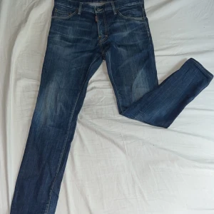 Blå jeansbyxor från Dsquared2 - Säljer ett par klassiska blå jeans från Dsquared2 med snygga slitningar och raka ben. Jeansen har fem fickor, gylf med dragkedja och knapp samt tydlig röd Dsquared2-lapp bak. Perfekta för dig som gillar stilrena jeans med premiumkänsla. Ny pris 6500kr pris kan diskuteras 