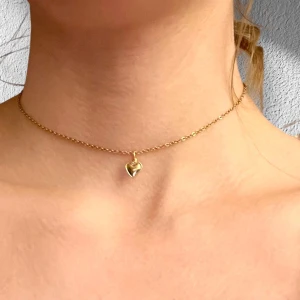 Choker guldhjärta halsband med litet hjärta - Ett litet guldigt hjärta trätt på en kortare kedja i guldimitation som är justerbar 35-40 cm. Berlocken är ganska tunn i materialet. 
