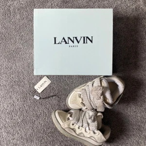 Lanvin sneakers med breda snören - Lanvin sneakers i beige med extra breda, mönstrade snören och rund tå. Skorna har en chunky sula och är tillverkade i skinn och syntet. Klassisk Lanvin-logga på plösen och innersulan. Snygg och unik design från Paris.