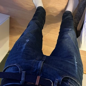 Mörkblå jeans från Pull&Bear, strl 38 - Säljer ett par mörkblå jeans från Pull&Bear i klassisk femficksmodell. Jeansen har en snygg tvätt med lätt slitna detaljer och medföljande mörkblått bälte. Modellen är rak och passar perfekt till en avslappnad stil.