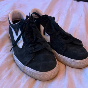 Mörkgröna warrior Shanghai 41/42 - Säljer ett par mörkgröna sneakers från Warrior med vit sula och vit sidodetalj. Skorna har snörning och röd gummisula undertill. Märkeslogga i gult på hälen och plösen. Klassisk och stilren modell.