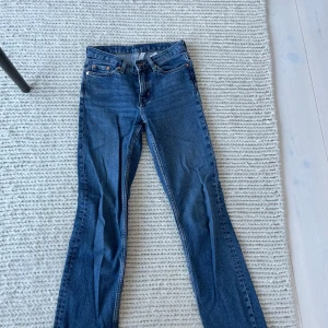 Blå bootcut jeans från Weekday - Säljer ett par klassiska blå bootcut jeans från Weekday. Jeansen har fem fickor, normal passform upptill och utsvängda ben. Tillverkade i jeansmaterial med snygga kontrastsömmar. Perfekta för dig som gillar en tidlös stil.