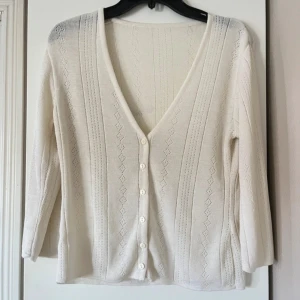 Vit stickad kofta med knappar - Säljer en söt vit stickad kofta med v-ringning och fina mönstrade detaljer i typ ”spets”. 