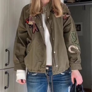 Grön jacka  - Säljer en olivgrön bomberjacka med snygga broderade detaljer som fågel, blomma och orm på bröst och ärm. Jackan har dragkedja, knappar och snörning nertill för en cool look. Passformen är loose och materialet känns som bomull eller polyester. Skriv privat för fler bilder 🥰