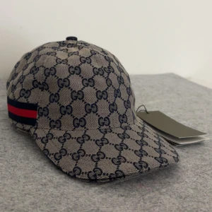 Beige gucci keps - Skriv dm för video eller prisförslag .Säljer en beige keps från Gucci med klassiskt GG-monogram i mörkblått och röd-blå rand på sidan. Justerbart spänne bak i svart skinn. Perfekt accessoar för en trendig look. Strolek ”M”