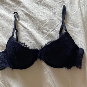 Mörkblå spets-bh från H&M - Säljer en mörkblå bh från H&M med vacker spetsdetalj och justerbara axelband. Bh:n har bygel och lätt vaddering för extra stöd. Perfekt för dig som vill ha något både snyggt och bekvämt under kläderna.