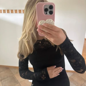 Svart spetsblus med lång ärm - Supersnygg svart blus med transparenta spetsärmar och detaljer upptill. Tight passform som framhäver figuren och ger en elegant vibe. Perfekt att styla med jeans eller kjol för en trendig look.