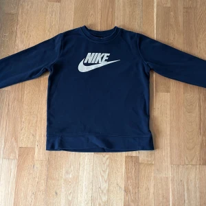 Svart Nike tröja med guldfärgad logga - Tja! Säljer en snygg svart tjocktröja från Nike med en stor guldfärgad logga på bröstet. Den är mjuk och len, perfekt för dig som vill ha en avslappnad och sportig stil