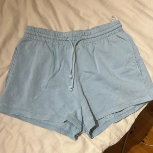 Shorts - Gina Tricot - Ljusblåa shorts från Gina Tricot med elastisk midja och snörning. De är tillverkade i mjuk bomull och har en loose fit som gör dem perfekta för varma dagar. Enkla att matcha och riktigt sköna att ha på sig hela sommaren (eller att sova i). De har blivit lite missfärgade men inget som syns särskilt mycket.
