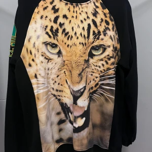 Adidas sweatshirt med leopardtryck - Svart Adidas sweatshirt med stort leopardansikte framtill och broderad grön-gul Adidaslogga på ärmen. Tröjan har lång ärm och är gjord i mjuk bomull. Perfekt statement piece för dig som vill sticka ut med djurprint och coola detaljer.