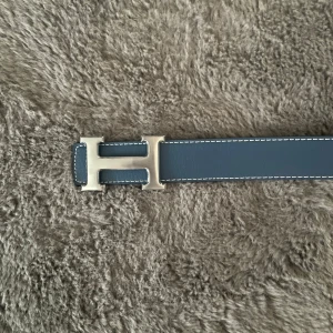 H bälte  - Snyggt svart bälte från H med ett stort, silverfärgat H-spänne. Bältet har vita sömmar längs kanterna som ger en stilren kontrast. Perfekt accessoar för att lyfta din outfit. Du får med armbandet också!