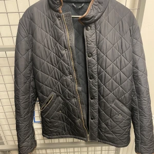 Mörkblå quiltad jacka med dragkedja och knappar - Snygg mörkblå quiltad jacka med både dragkedja och knappar framtill. Jackan har två snedställda fickor med dragkedja och hög krage. Perfekt för kyligare dagar och ger en stilren look. Hyfsat stor i storlek