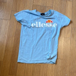 Ljusblå t-shirt från Ellesse - Säljer en ljusblå t-shirt från Ellesse med stort vitt tryck och logga framtill. Klassisk rund hals och korta ärmar. Perfekt för en sportig och avslappnad stil.