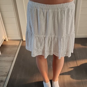 Vit volangkjol från Hailys - Säljer en söt vit kjol från Hailys med broderade detaljer och volang nertill. Kjolen har resår i midjan och är i en luftig bomullskvalitet, perfekt för varma dagar. Den har ett romantiskt och somrigt uttryck.