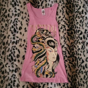 Rosa Ed Hardy linne med tryck - Säljer en rosa one size linne från Ed Hardy med stort färgglatt drak- och rosmotiv fram och bak.guldiga detaljer samt texten 'Tattoo' och 'Ed Hardy'.. Skriv om du har frågor😊