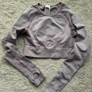 Ljuslila croppad träningströja från Gymshark - Säljer en ljuslila croppad långärmad träningströja från Gymshark. Tröjan har tumhål i ärmsluten och är tillverkad i ett stretchigt syntetmaterial. Perfekt för gym eller annan träning!