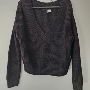 Svart stickad v-ringad tröja från H&M - Säljer en svart stickad tröja från H&M med djup v-ringning. Tröjan har lång ärm och är tillverkad i 100% akryl. Perfekt att styla med jeans eller kjol för en avslappnad look. Noppror finns
