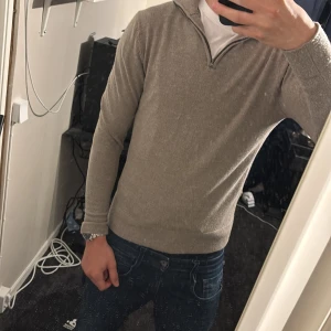 Beige halvzip-tröja från These Glory Days - Säljer en stilren beige halvzip-tröja från These Glory Days. Tröjan har lång ärm, hög krage med dragkedja och är tillverkad i mjukt material. Perfekt för lager-på-lager och passar till jeans tröjan är i merinoull nypris 1100-: använd fåtal gånger men säljer då den var lite för liten