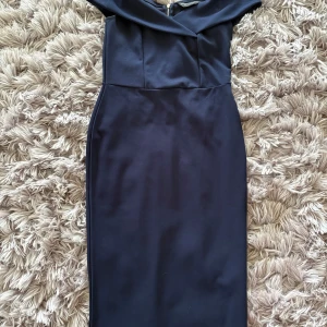 Marinblå offshoulder klänning från Dorothy Perkins - Säljer en elegant marinblå klänning från Dorothy Perkins med offshoulder-skärning och guldfärgad dragkedja bak. Klänningen har en figurnära passform och är perfekt för festliga tillfällen.