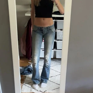 Lågmidjade bootcut jeans  - Säljer ett par ljusblå jeans med bootcut passform och slitna detaljer framtill. Jeansen är lågmidjade Perfekta för en avslappnad och trendig look.