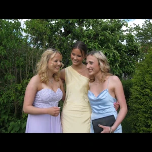 Ljusgul långklänning med oneshoulder - Säljer en elegant långklänning i champagnefärgat satinmaterial. Klänningen har en stilren oneshoulder-design med en liten knutdetalj på axeln. Passformen är slim och tyget har en lyxig glans. Perfekt för bal eller fest.