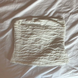 Vit strukturerad tubtopp - Säljer en vit tubtopp med vågig struktur i tyget. Toppen är axelbandslös och har en lätt figurnära passform. Perfekt att styla med jeans eller kjol för en trendig look. Använd ungefär 4 gånger💕
