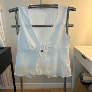 Vit ribbad linnetopp från lager 157 - Supersöt vit linnetopp från lager 157 med ribbad struktur och v-ringning. Toppen har knyt framtill och är ärmlös, perfekt för varma dagar. Lätt och luftig känsla, passar till både jeans och kjol. Säljer då den inte kommer till användning längre!