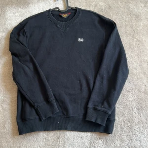 Svart sweatshirt från Lee ( pris kan diskuteras ) - Klassisk svart sweatshirt från Lee med broderad logga på bröstet. Tröjan har rund halsringning, ribbade muddar vid ärmslut och nederkant samt en relaxed passform. Perfekt för en enkel och stilren look.