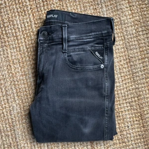 Svarta Replay Hyperflex jeans - Säljer ett par svarta Replay Hyperflex jeans, modell Bronny. Jeansen har klassisk femficksdesign, dragkedja och är tillverkade i stretchigt material för extra komfort. Perfekta för dig som vill ha snygga och bekväma jeans med modern passform. Skick 10 av 10. Hör av er vid fundering 