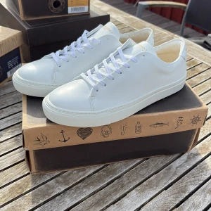 Vita sneakers från Sneaky Steve - Säljer ett par stilrena vita sneakers från Sneaky Steve med klassisk design. Skorna har snörning, rund tå och platt sula. Perfekta för dig som gillar minimalistisk stil och vill ha ett par fräscha skor till vardags.