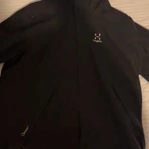 Svart vindjacka från Haglöfs - Säljer en svart vindjacka från Haglöfs med dragkedja. Jackan är långärmad och tillverkad i ett syntetmaterial. Perfekt för utomhusaktiviteter och skyddar mot vind och regn. Pris går att diskuteras vid snabb intresse 