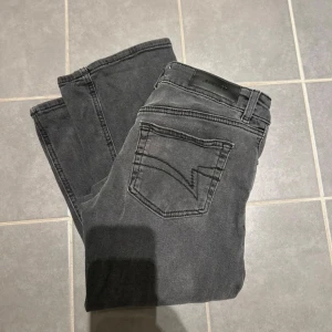 Gråa jeans från Junkyard  - Snygga grå jeansbyxor från Junkyard med en klassisk femficksdesign. Byxorna har en diskret tvättad look och en bekväm passform. Perfekta för en stilren vardagslook. Jeansen är i storlek xs.