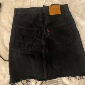 Svart jeanskjol från Levi's - Snygg svart jeanskjol från Levi's med en rå kant och knappar framtill. Säljer då den tyvärr är för liten.
