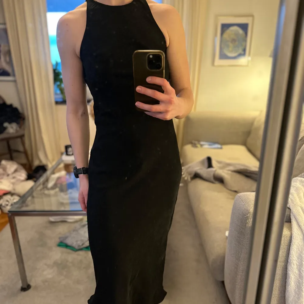 Snygg svart klänning från Zara i en tight passform. Klänningen är ärmlös och har en elegant design med en knappdetalj i nacken. Slutar på vaderna och i satinmaterial.. Mekot.