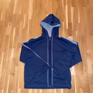 Blå huvtröja från Champion - Säljer en blå huvtröja från Champion med dragkedja och grå detaljer. Tröjan har långa ärmar och en bekväm huva. Perfekt för en avslappnad stil.